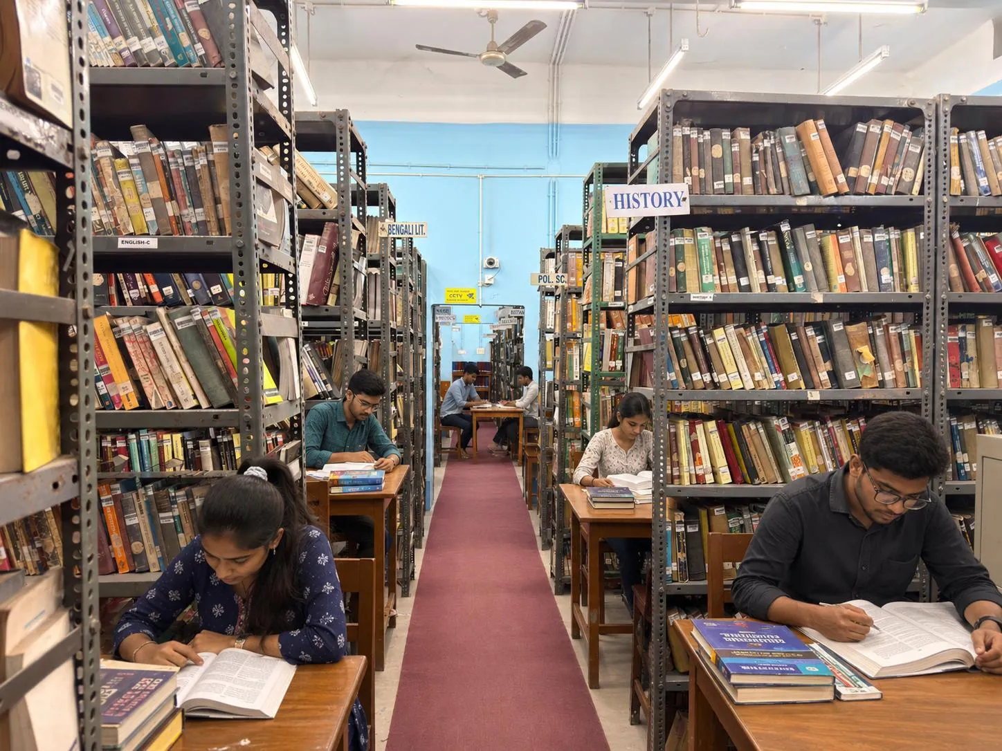 Students reading at desks between book stacks in the Raiganj University central library
